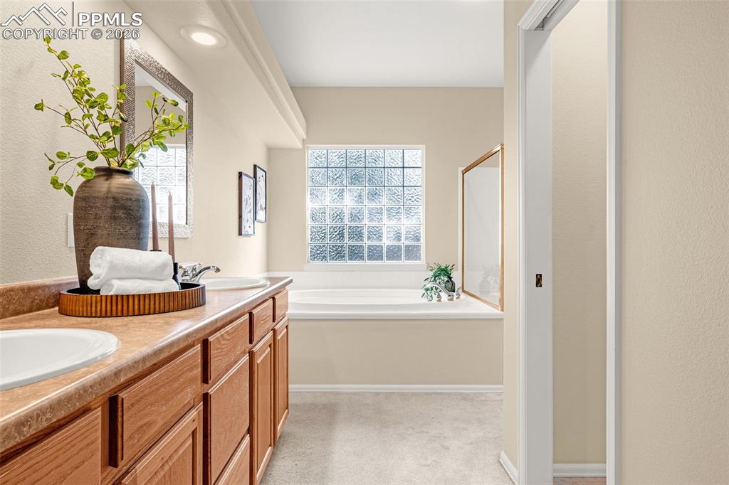 Image 22 of 40: This bathroom features a double vanity with wooden cabinetry, a large batht