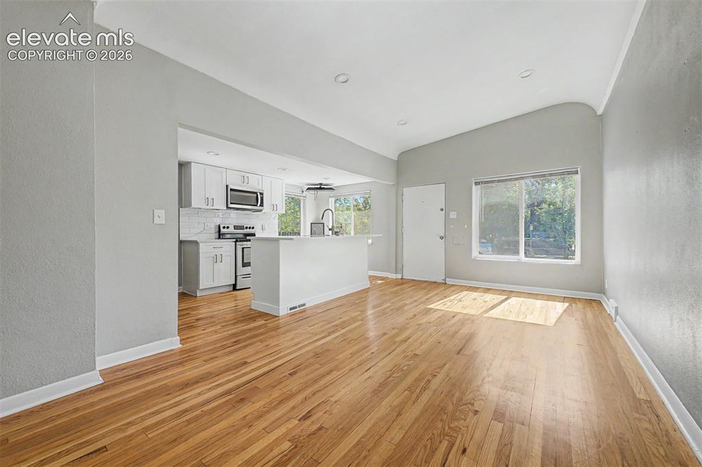 Image 11 of 40: Modern kitchen featuring wood-finish flooring, white cabinetry with gold-to