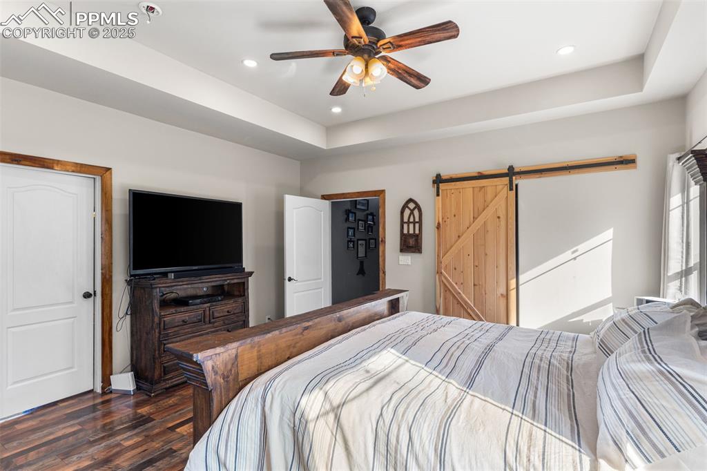 Image 13 of 46: Bedroom featuring a barn door, dark wood-style floors, recessed lighting, a