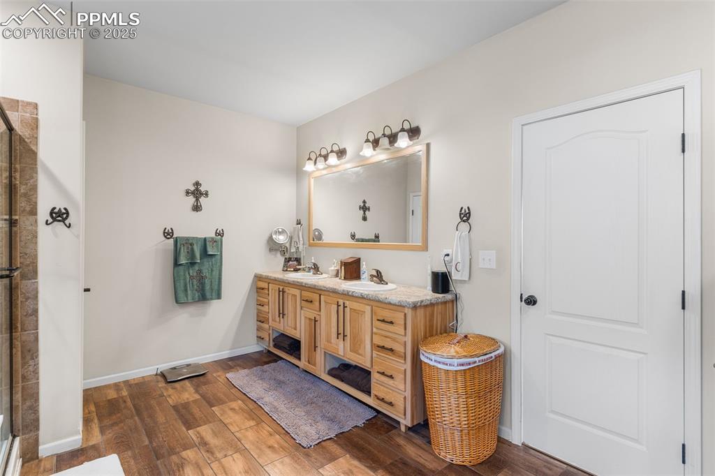 Image 14 of 46: Bathroom featuring wood finished floors, double vanity, and a tile shower