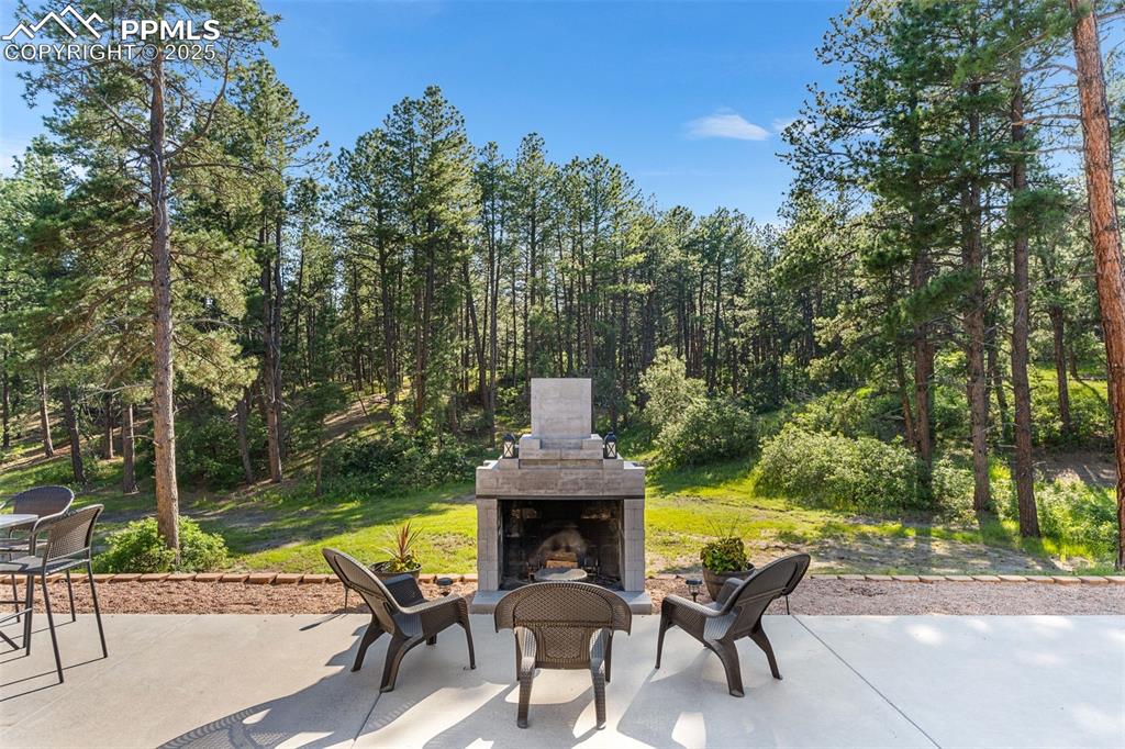 Image 32 of 46: View of patio / terrace with an outdoor stone fireplace and a wooded view