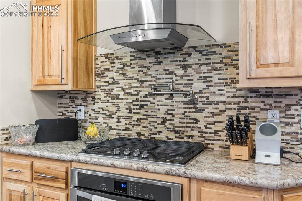 Image 7 of 46: Kitchen with wall chimney exhaust hood, light brown cabinets, decorative ba