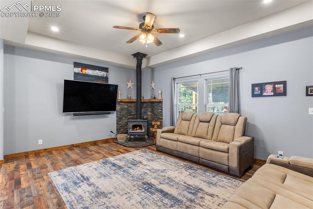 Image 8 of 46: Living area with a wood stove, ceiling fan, wood-type flooring, recessed li
