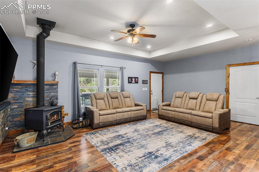 Image 9 of 46: Living area featuring a wood stove, ceiling fan, wood finished floors, a ra