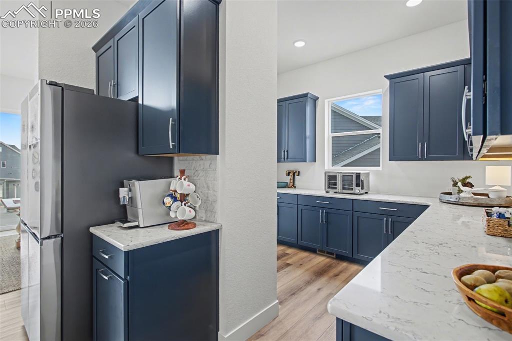 Image 14 of 39: Kitchen featuring blue cabinetry, light stone countertops, and light wood-t