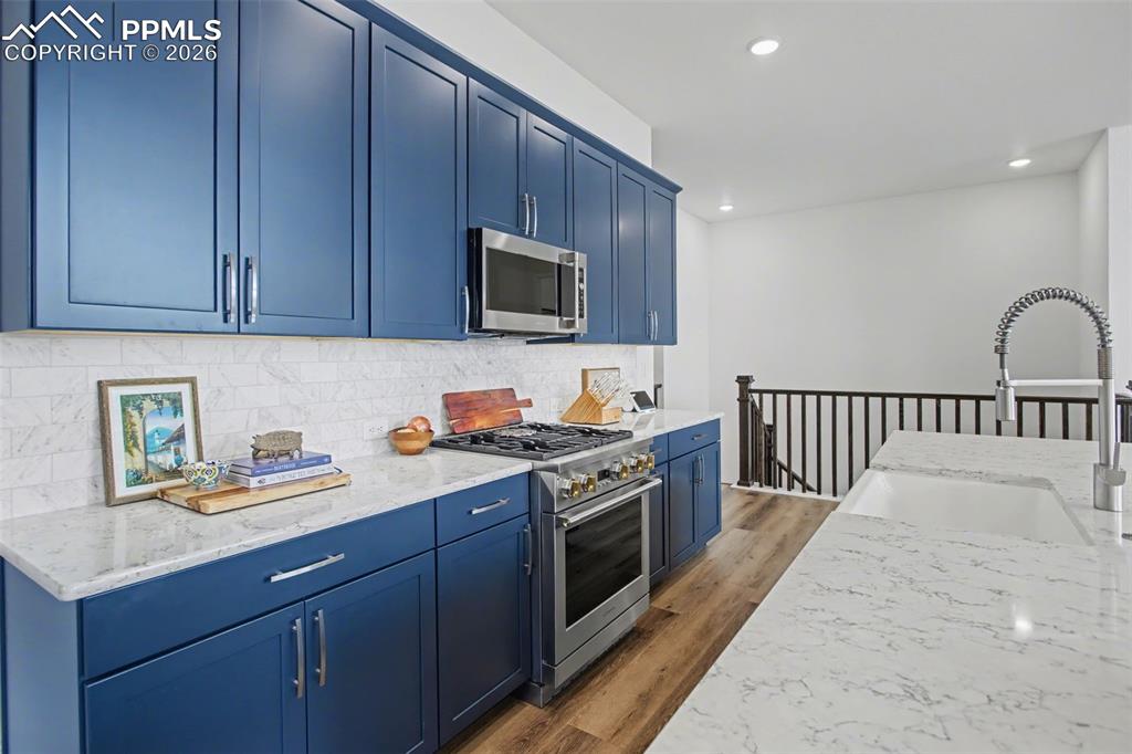 Image 17 of 39: Kitchen featuring blue cabinets, stainless steel appliances, light stone co