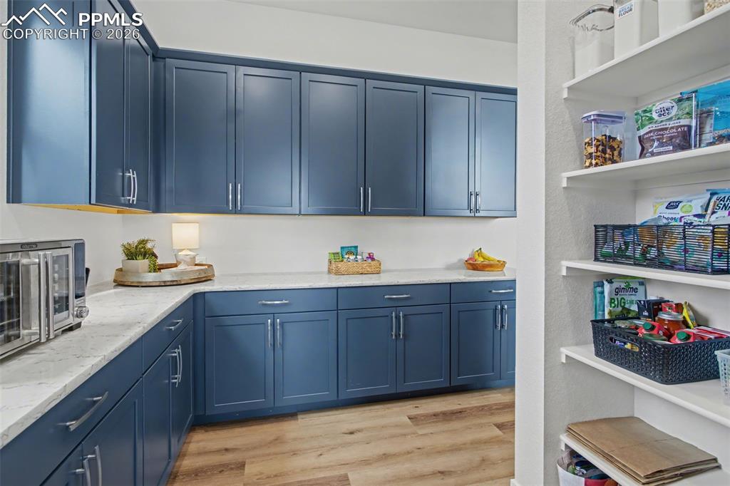 Image 18 of 39: Kitchen with blue cabinets, light wood-style floors, and light stone counte