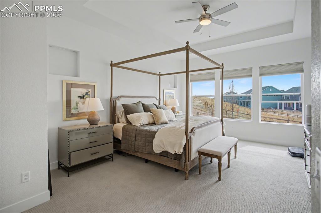 Image 22 of 39: Bedroom with light colored carpet, a ceiling fan, and a tray ceiling