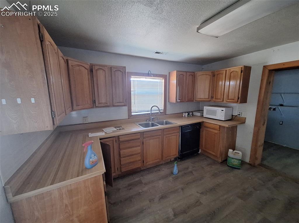 Image 3 of 24: Kitchen with dark wood-type flooring, a textured ceiling, brown cabinetry,