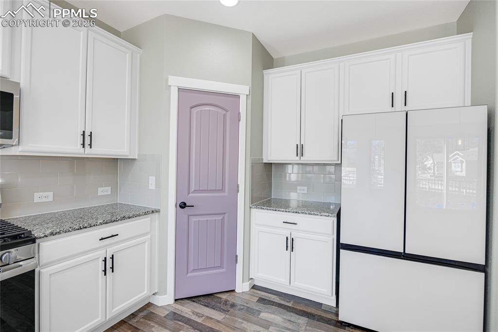 Image 12 of 50: The kitchen features white cabinetry with black hardware, granite counterto