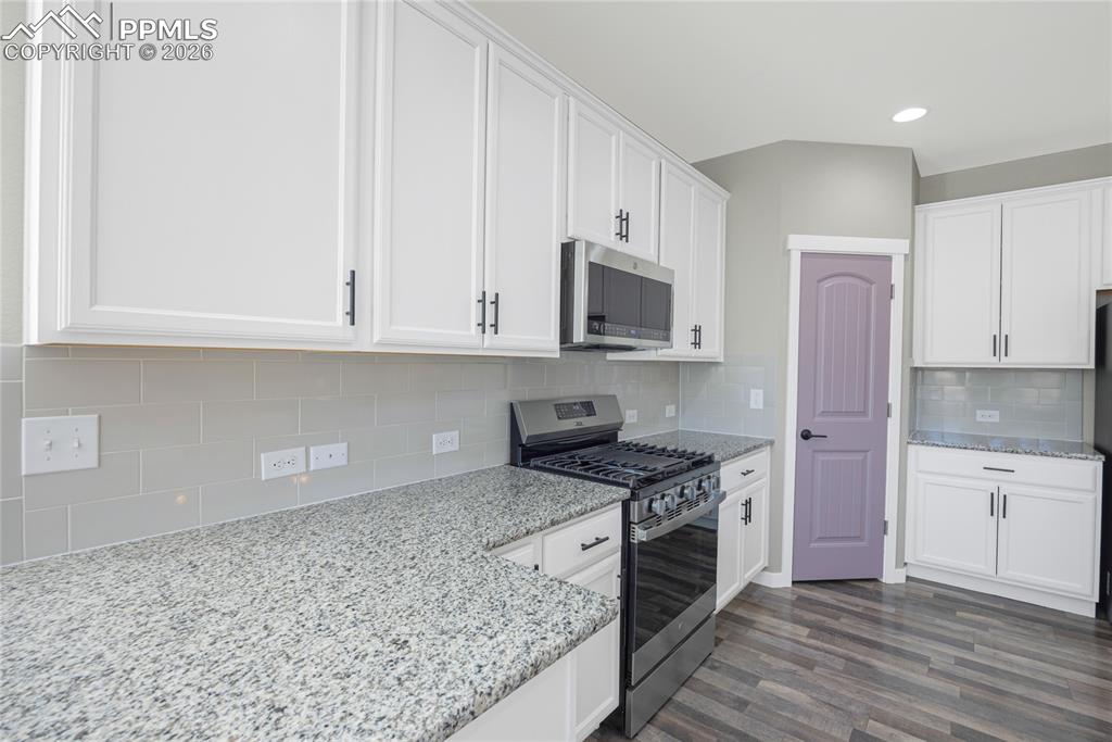Image 13 of 50: The kitchen features white cabinetry, granite countertops, a gas range, and