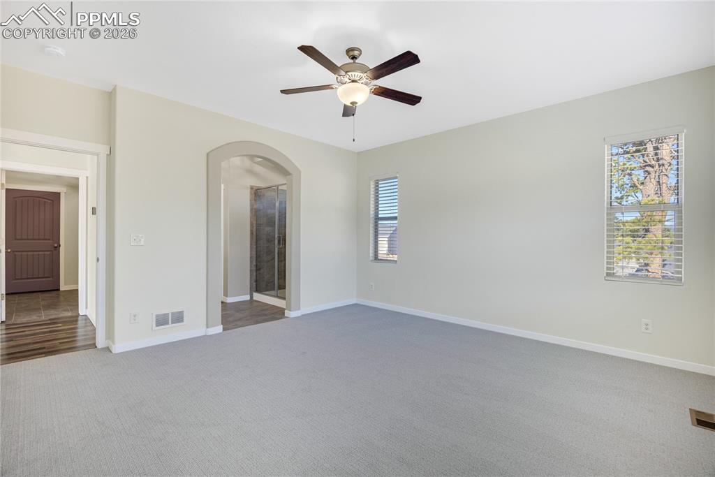 Image 27 of 50: Spacious room with light-colored carpeting, a ceiling fan, and windows prov