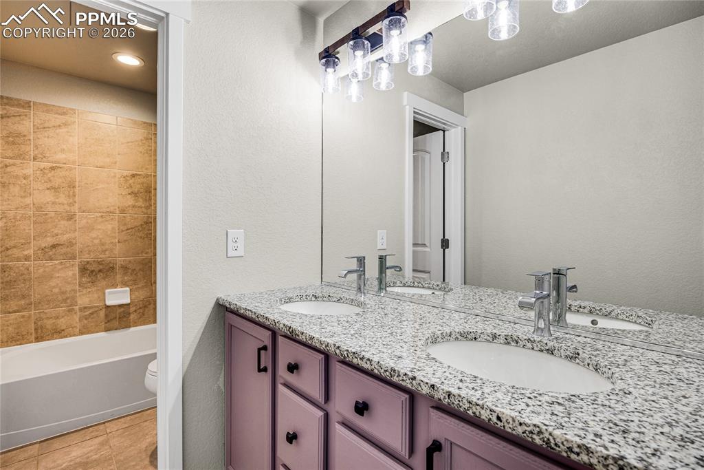 Image 29 of 50: Bathroom featuring a double vanity with a speckled countertop and purple ca