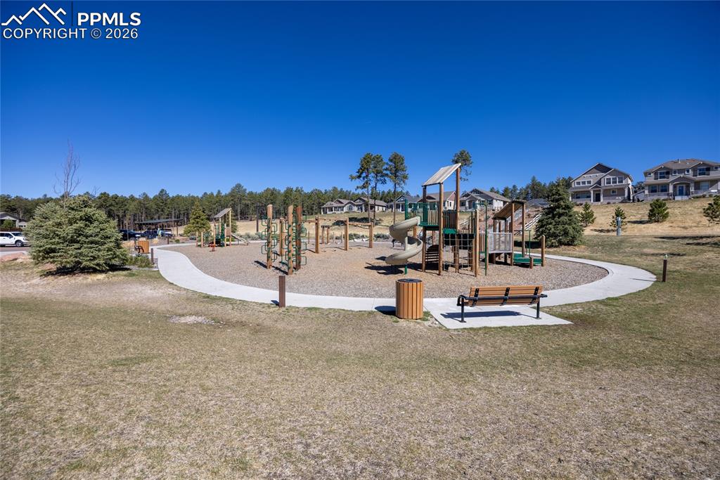 Image 41 of 50: The community playground features play structures, a bench, and a paved pat