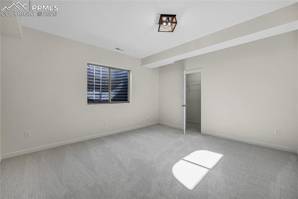 Image 44 of 50: This room features light gray carpet, a window with horizontal blinds, and 