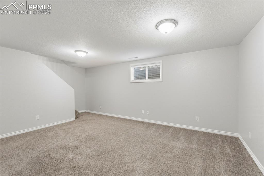Image 24 of 48: Basement with light colored carpet and a textured ceiling