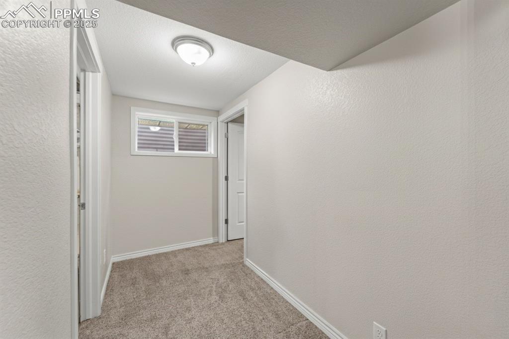 Image 32 of 48: Hallway with light colored carpet, a textured wall, and a textured ceiling