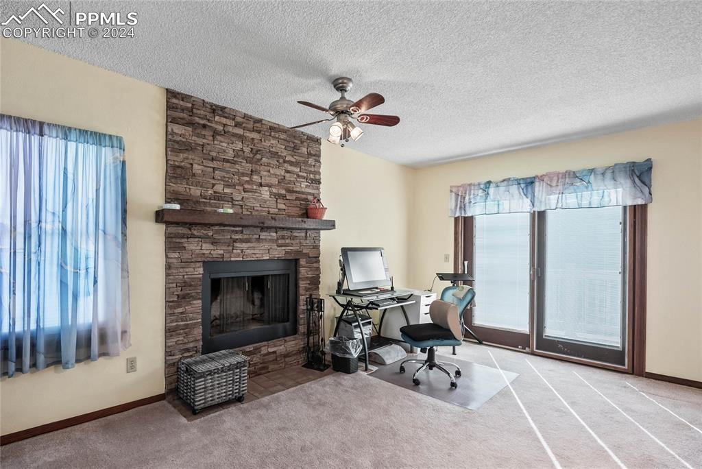 Image 25 of 48: Primary Suite Office featuring a stone fireplace, light carpet, ceiling fan