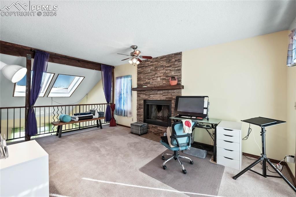 Image 26 of 48: Primary Suite Office with a skylight, ceiling fan, a fireplace, and carpet 