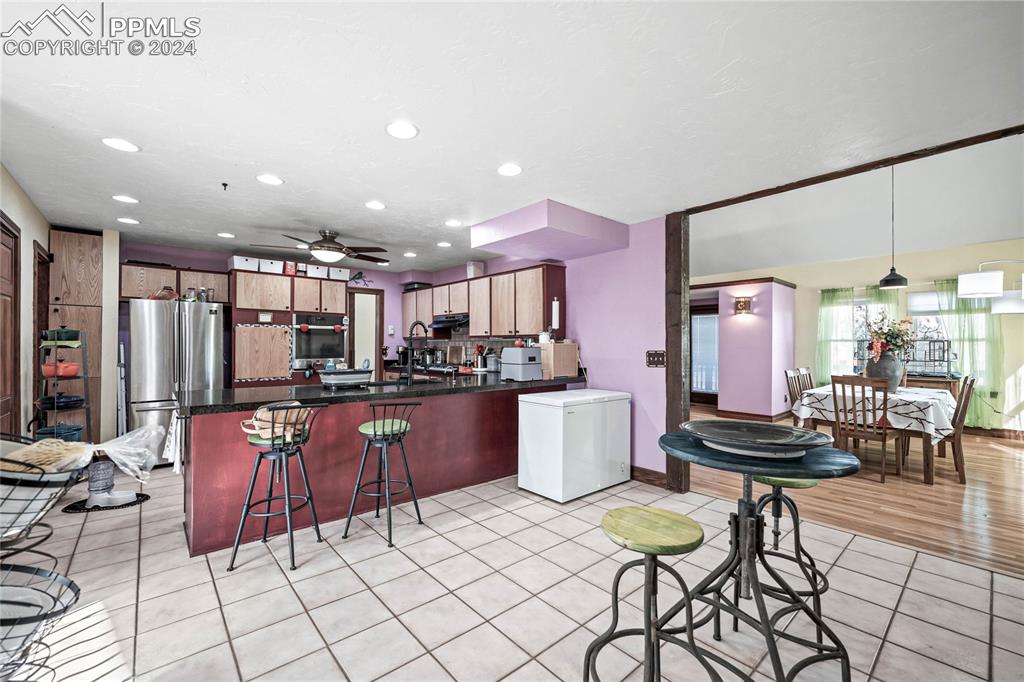 Image 32 of 48: Kitchen with ceiling fan, hanging light fixtures, a kitchen breakfast bar, 