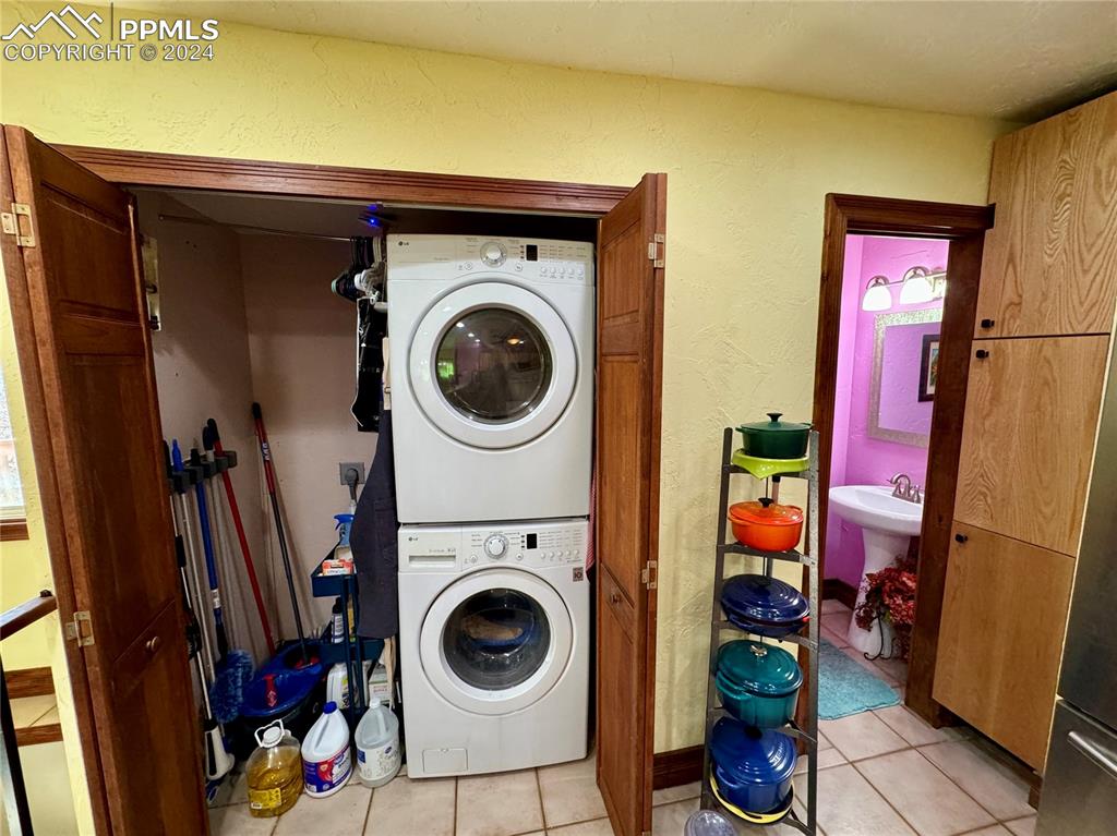Image 46 of 48: Clothes washing area with stacked washing maching and dryer and light tile 