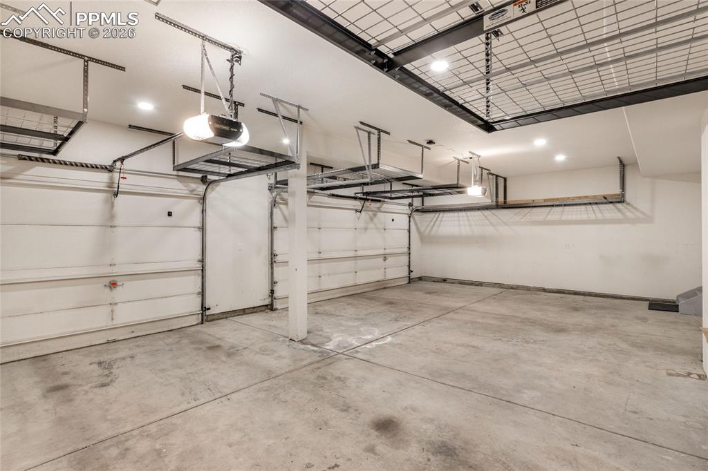 Image 16 of 35: Spacious 3 car garage with multiple overhead storage racks, two garage door