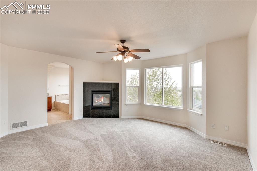 Image 18 of 35: Primary bedroom with corner fireplace featuring a dark tile surround, and b