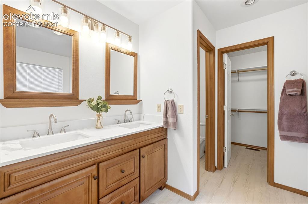 Image 13 of 32: Dual vanity with wood-finish cabinetry, white countertops, and integrated s