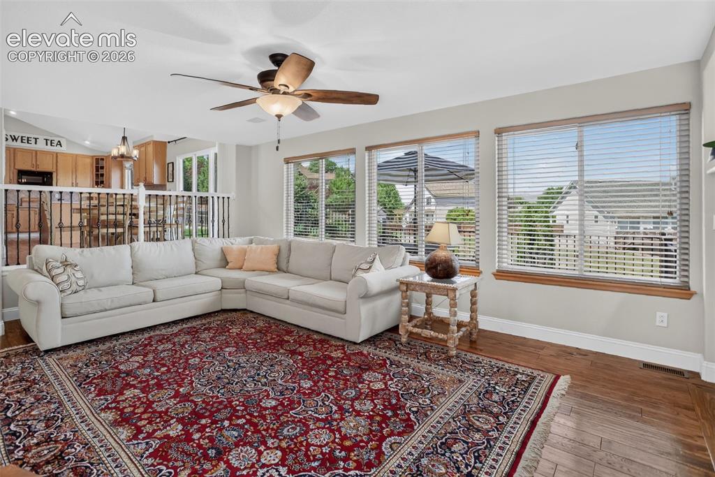 Image 21 of 49: Living area with wood-finish flooring, multiple windows, a ceiling fan, and