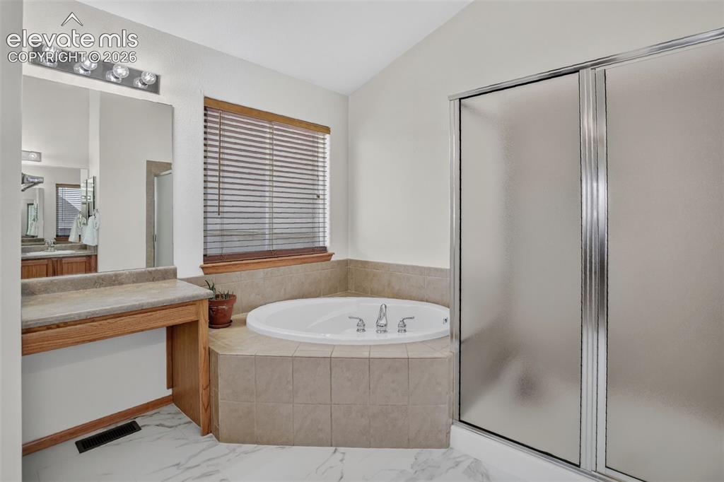 Image 32 of 49: Bathroom featuring a built-in corner bathtub with tiled surround, a separat