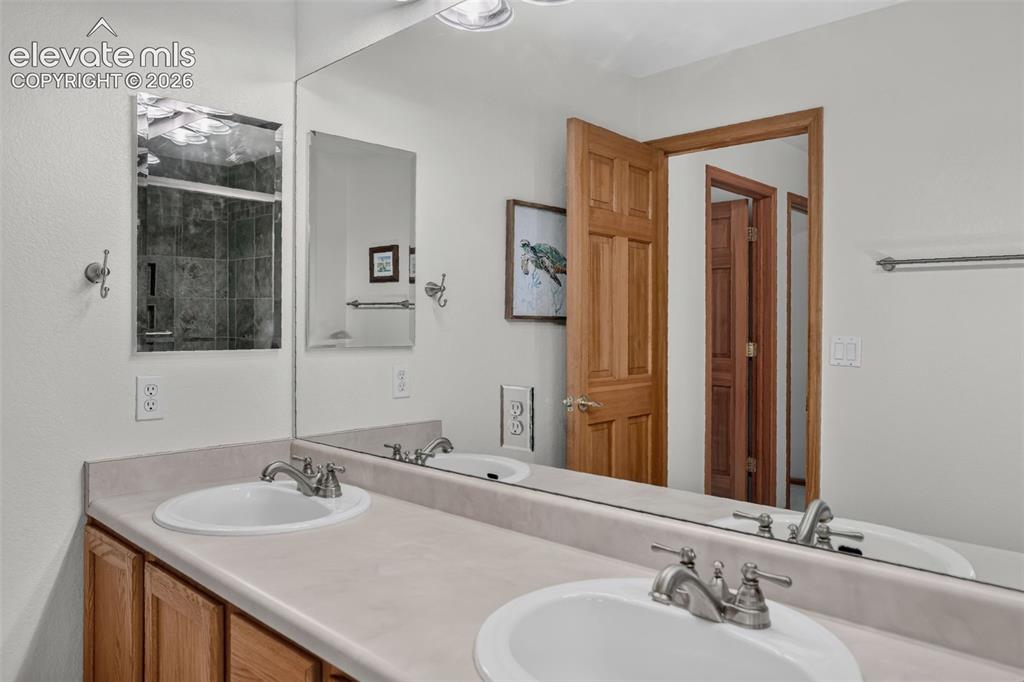 Image 37 of 49: Bathroom featuring a dual-sink vanity with light-toned countertops, wood-fi