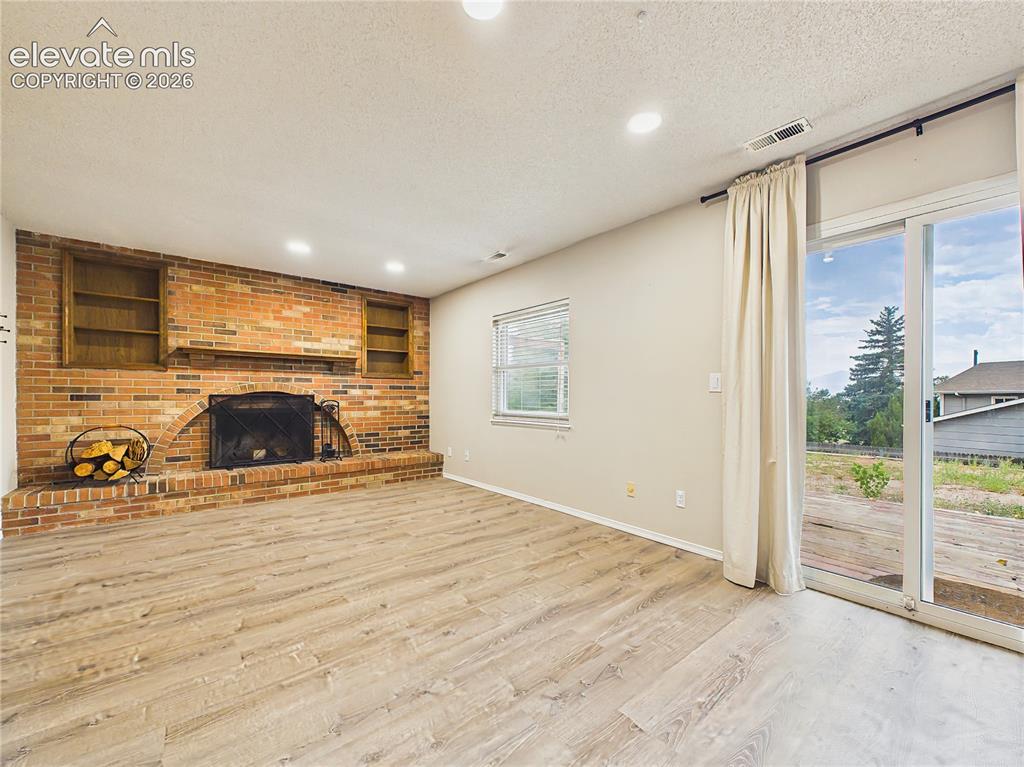 Image 23 of 50: Bright lower-level family room featuring a striking brick fireplace and sli