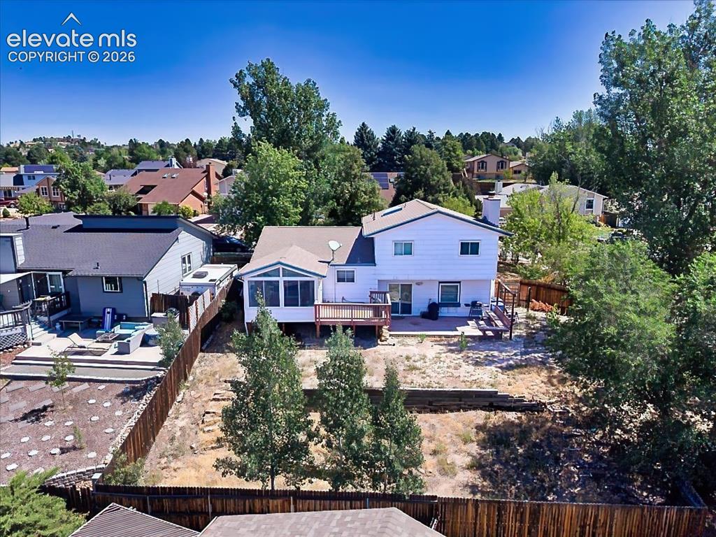 Image 47 of 50: Spacious fenced backyard featuring a large deck, enclosed sunroom, and matu