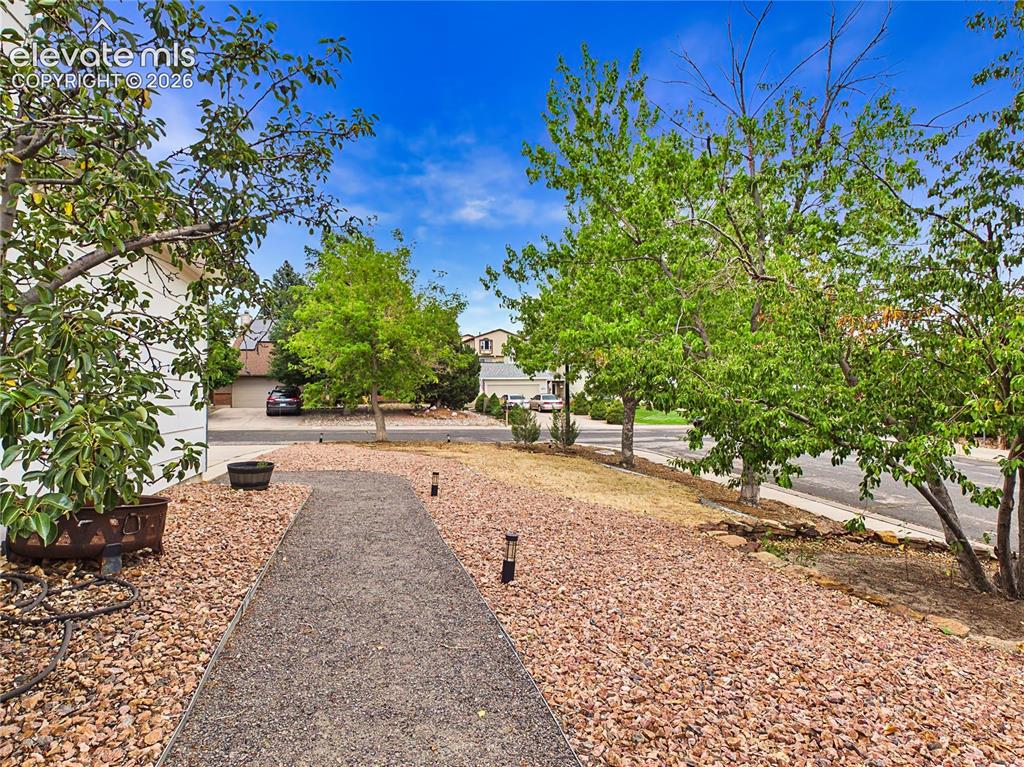 Image 48 of 50: Landscaped front yard with mature trees, decorative rock, and a welcoming w