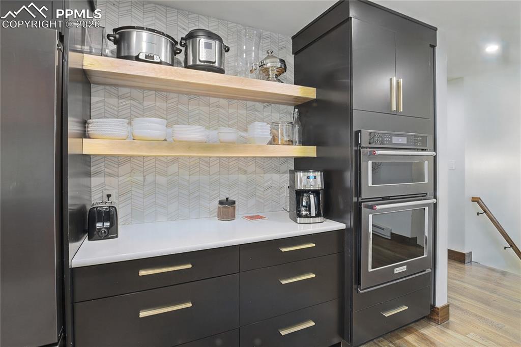 Image 12 of 50: Kitchen featuring open shelves, dark cabinetry, stainless steel appliances,