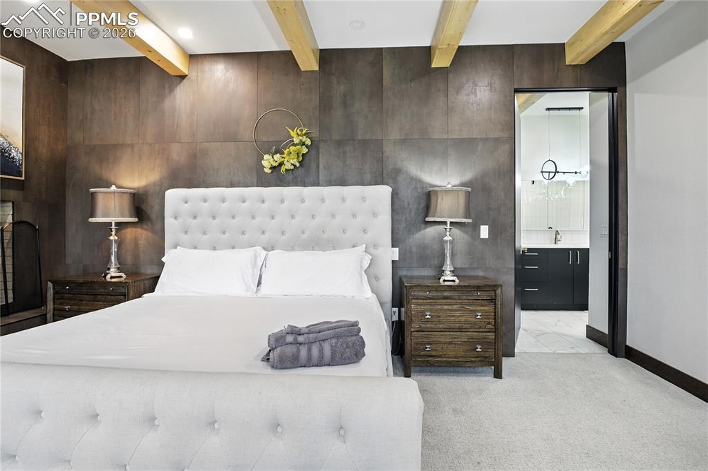 Image 25 of 50: Carpeted bedroom with beamed ceiling and wooden walls