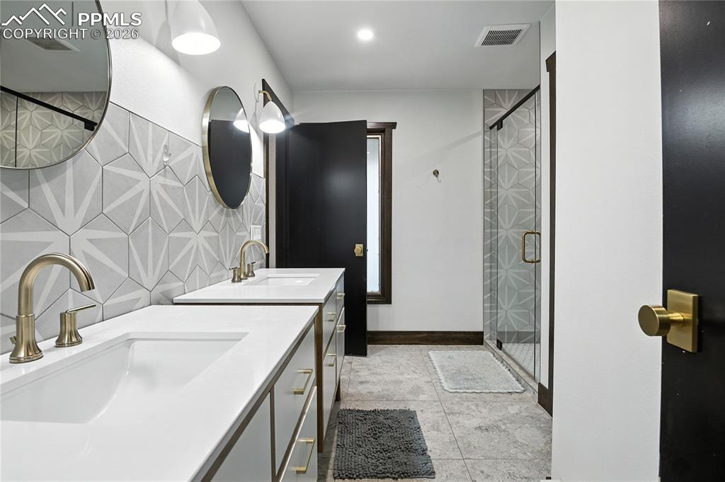 Image 42 of 50: Full bathroom featuring a stall shower, backsplash, two vanities, and light