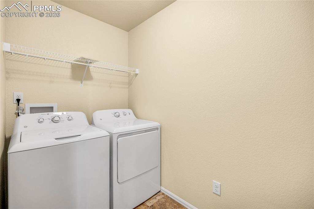 Image 27 of 32: Upstairs laundry area with full-size washer and dryer, plus overhead shelvi