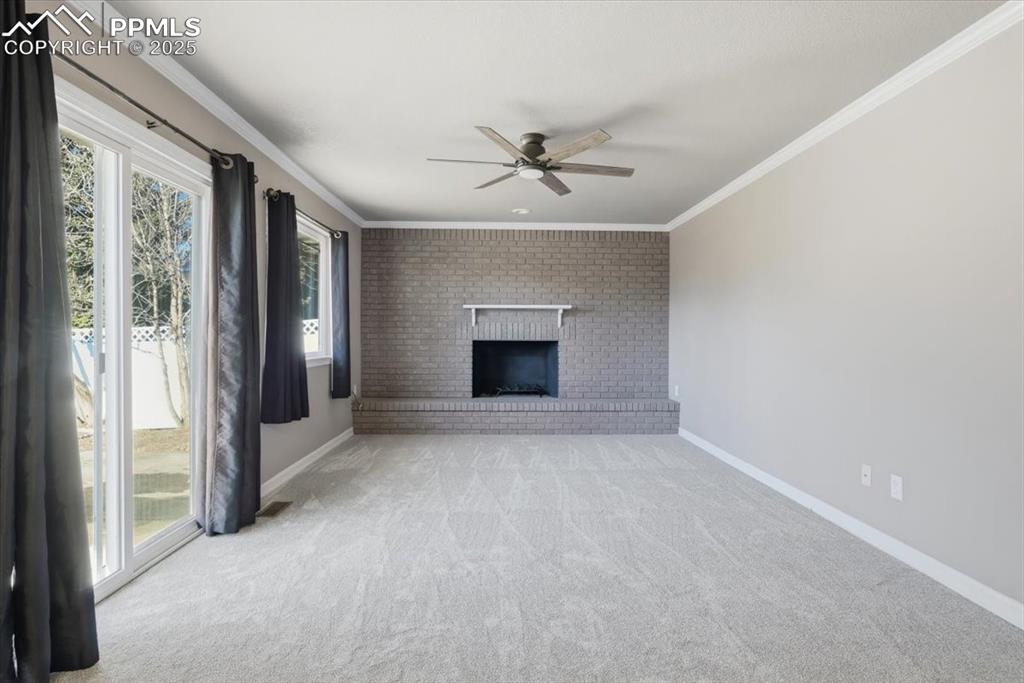 Image 16 of 48: Unfurnished living room with crown molding, light carpet, a brick fireplace