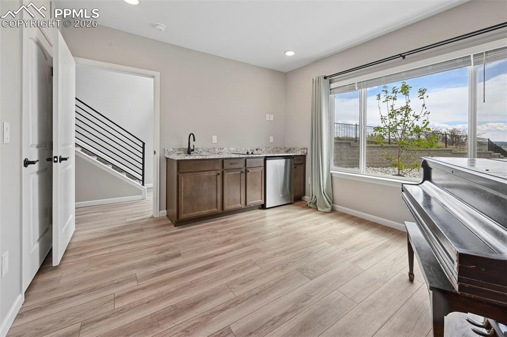 Image 13 of 42: Spacious room featuring wood-finish flooring, a built-in wet bar with dark 