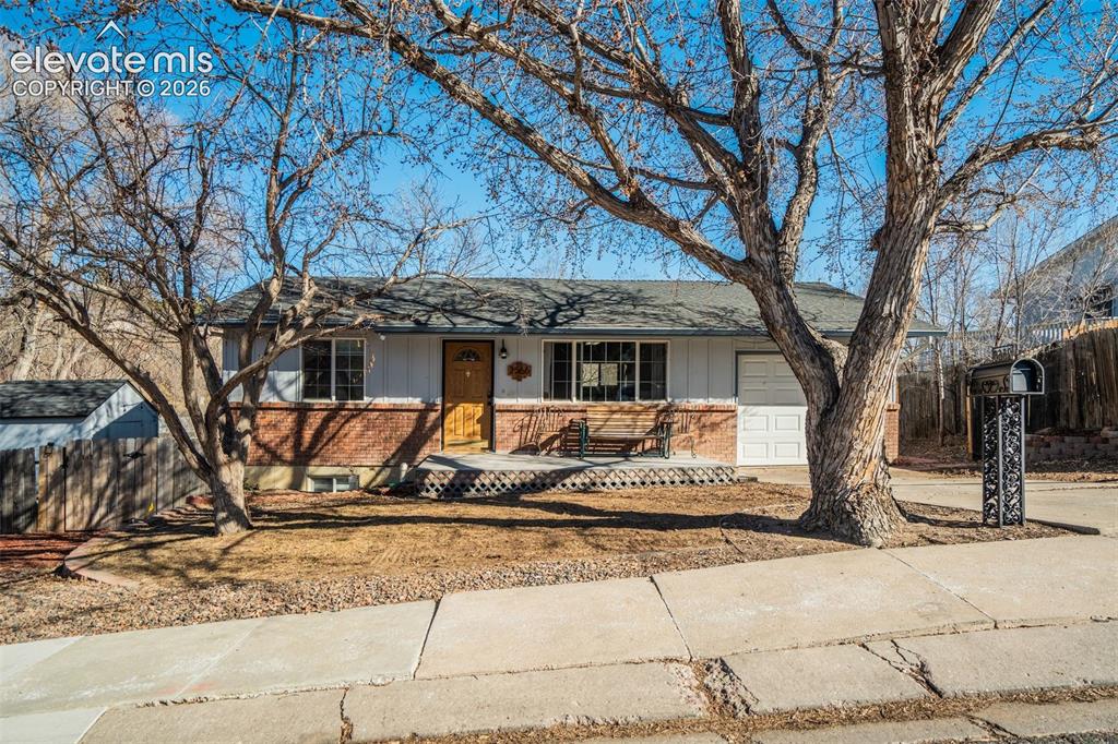 Caption: Ranch-style exterior with a brick and siding facade, covered entry porch, and mature trees