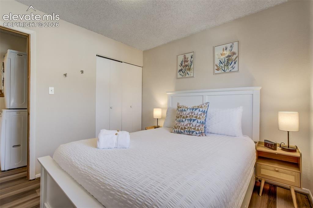 Image 18 of 50: Stacked washer and dryer unit, wood-finish flooring, white paneled headboar