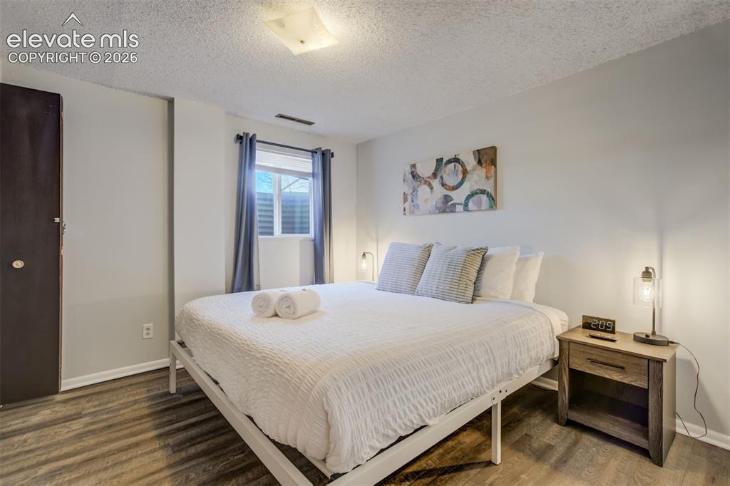 Image 28 of 50: Wood-finish flooring, white walls, and a window with blinds and curtains
