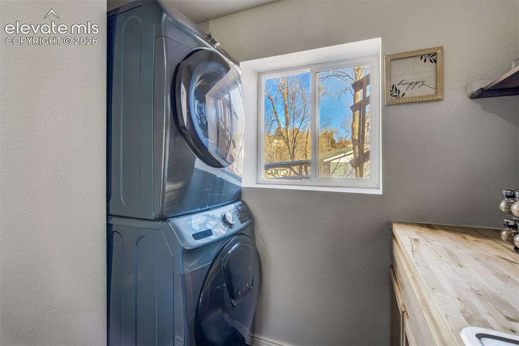 Image 35 of 50: Stacked laundry appliances, wood-finish countertop, and a white-framed wind