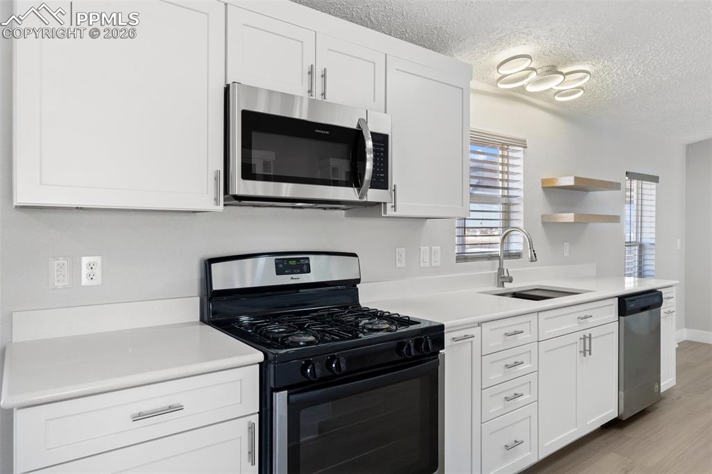 Image 22 of 50: Kitchen featuring stainless steel appliances, sink, white cabinets, and lig