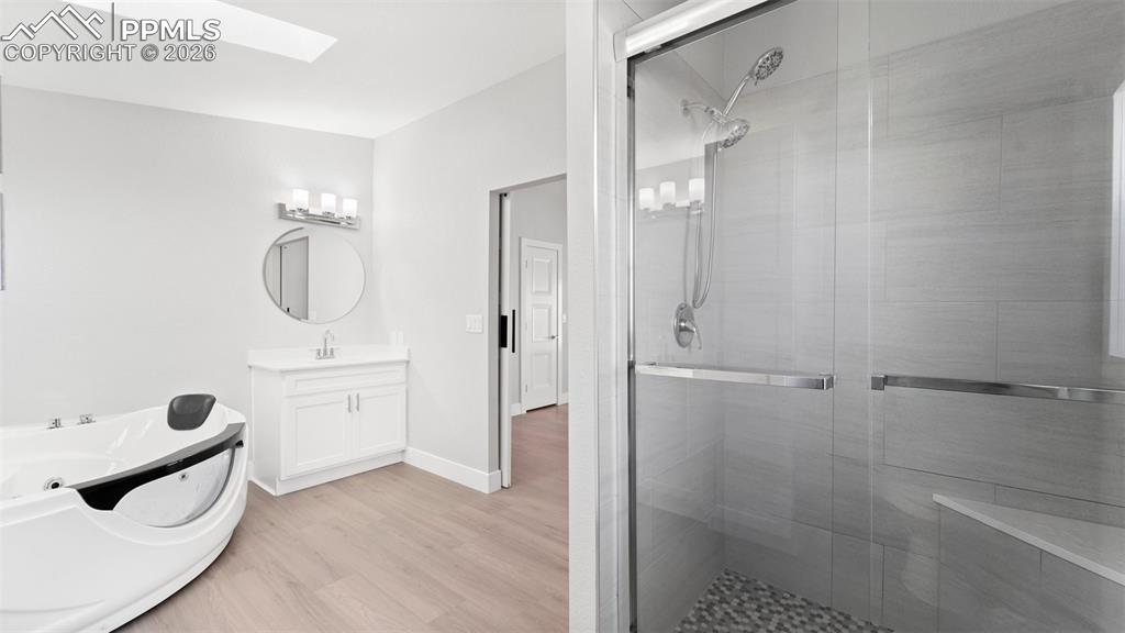 Image 29 of 50: Bathroom with vanity, a skylight, wood-type flooring, and a shower with sho