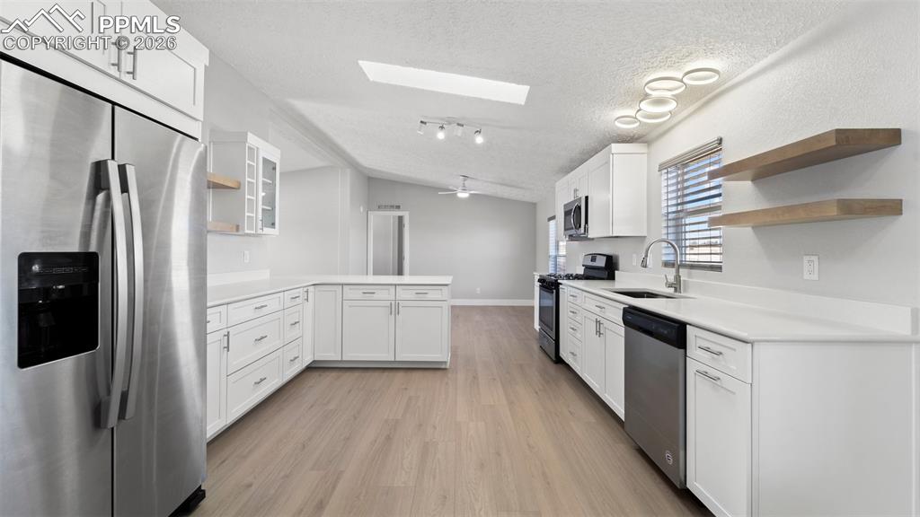 Image 34 of 50: Kitchen featuring sink, white cabinetry, lofted ceiling with skylight, stai