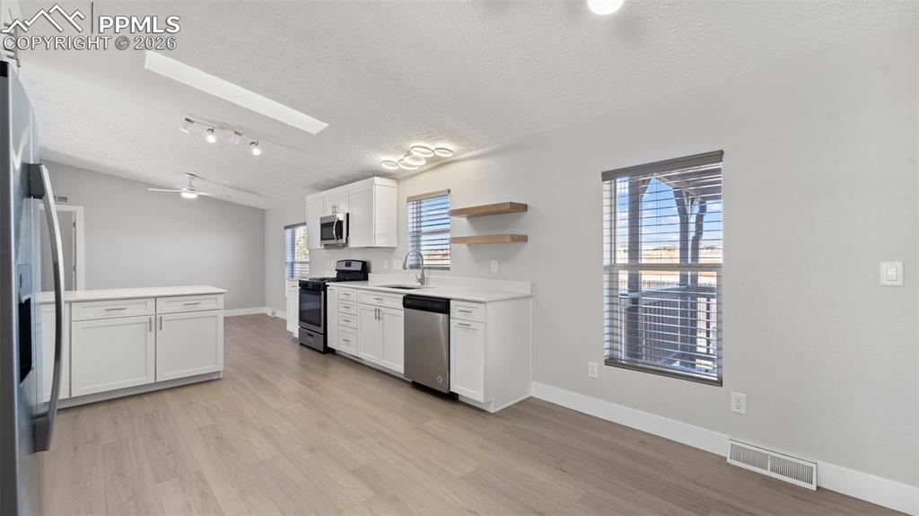 Image 43 of 50: Kitchen featuring stainless steel appliances, sink, white cabinets, and lig