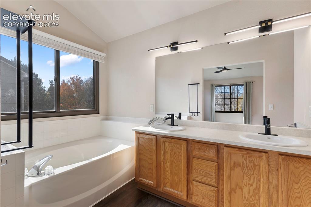 Image 20 of 38: Soaking tub with a large window, dual vanity with wood cabinetry, matte bla