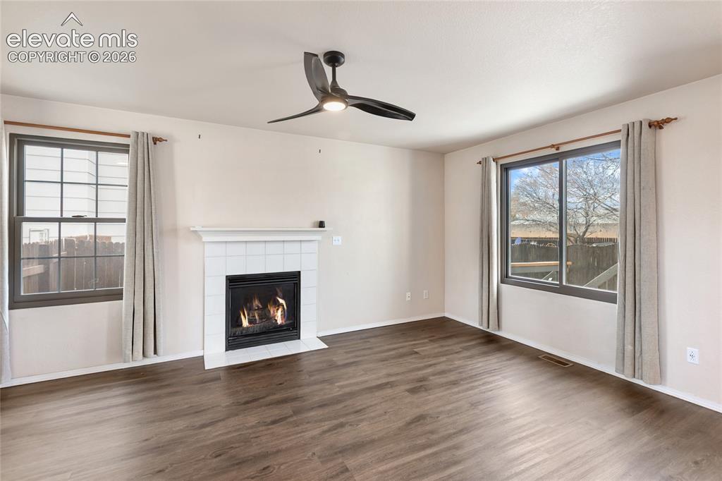 Image 7 of 38: Living area featuring wood-finish flooring, a white tiled fireplace with a 